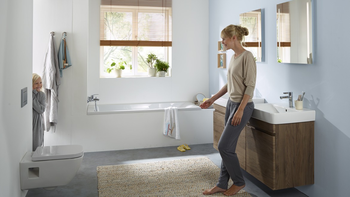 Femme et enfant debout dans une salle de bains familiale de la collection Geberit Renova (© Geberit)