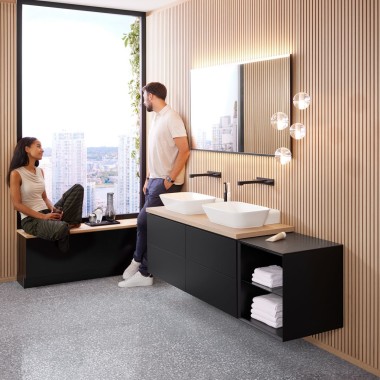 Femme assise sur le rebord d’une fenêtre parlant à un homme dans une salle de bains design, Geberit ONE