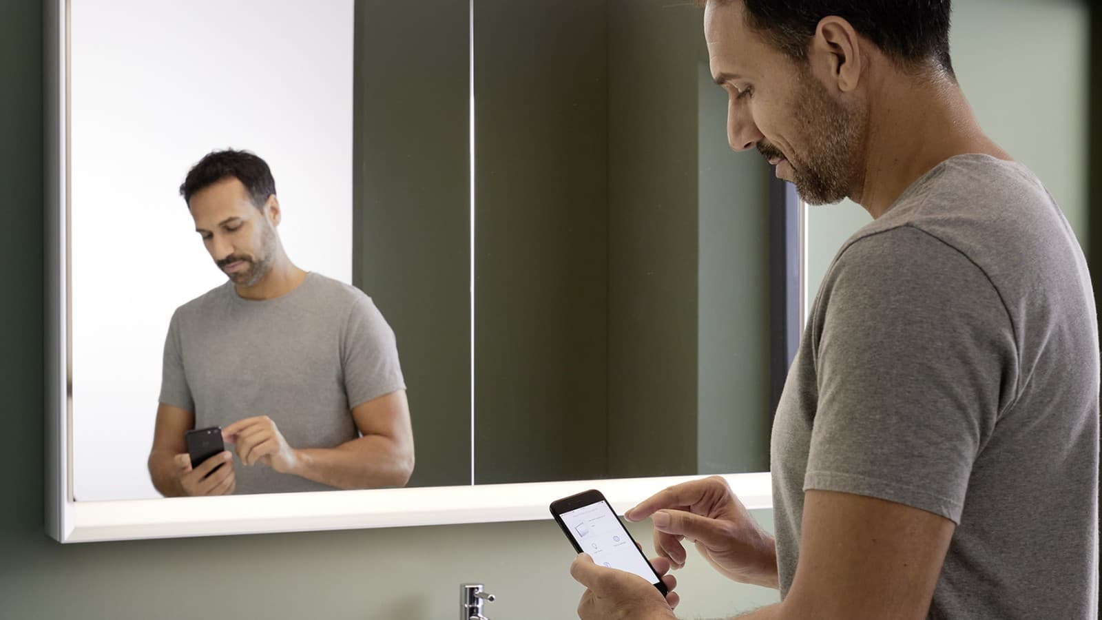 MANN contrôle les miroirs avec le concept d'éclairage Geberit ComfortLight avec son téléphone portable MANN contrôle les miroirs avec le concept d'éclairage Geberit ComfortLight avec son téléphone portable